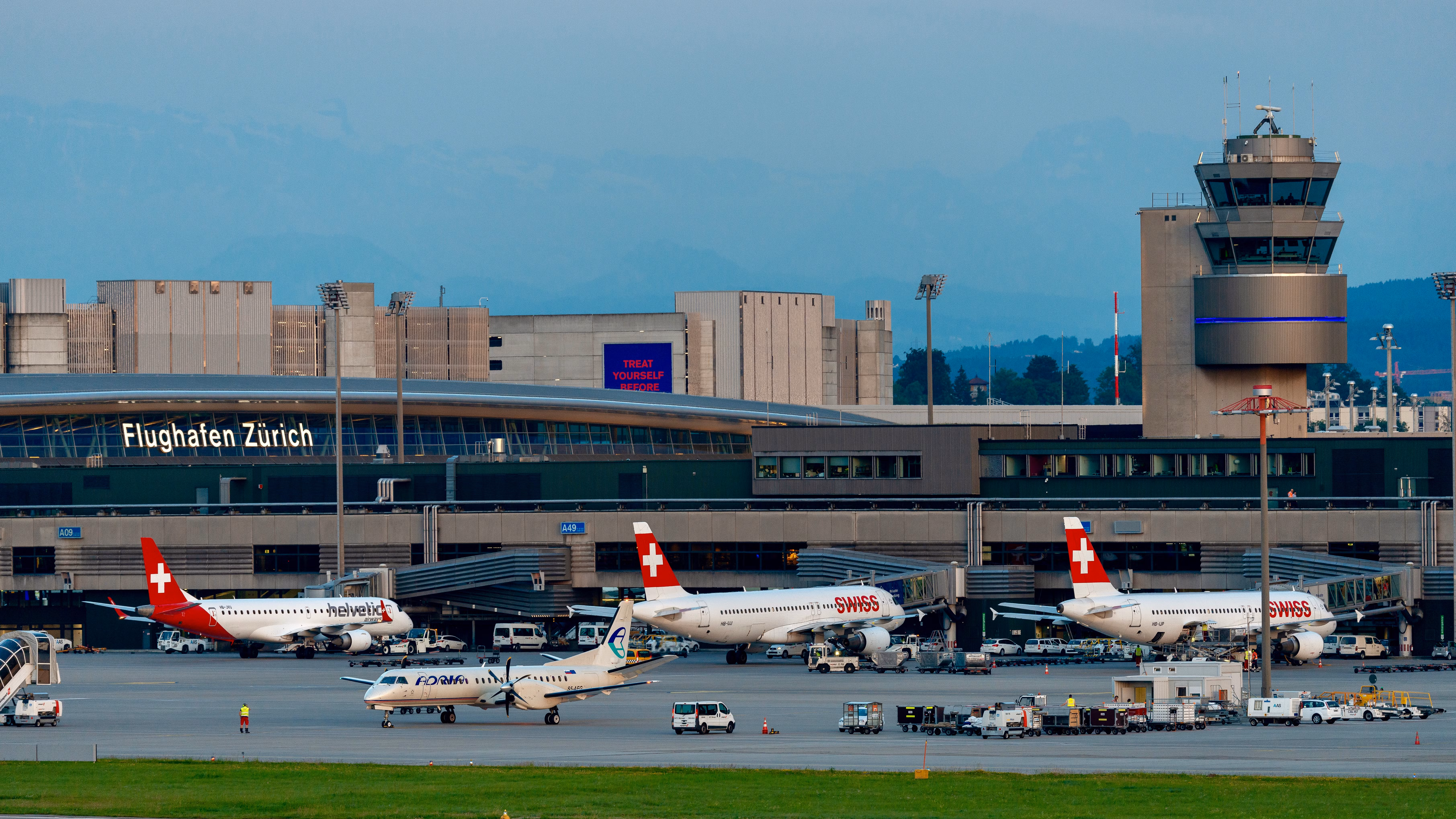 Zurich Flughafen apron showing Swiss and regional aircraft parked at gates with the control tower in the background